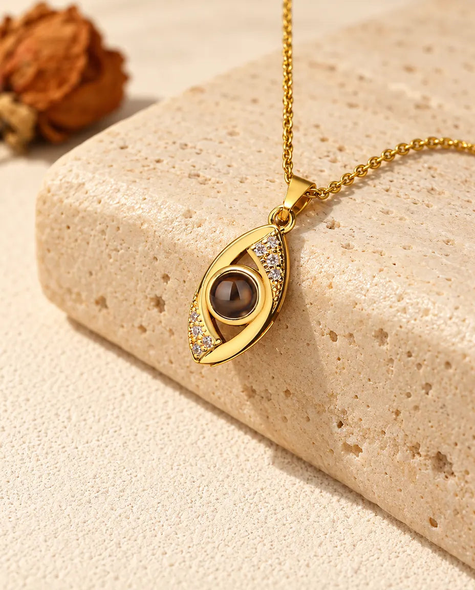 Goudkleurige ketting met het boze oog en foto erin, hangend over travertijn