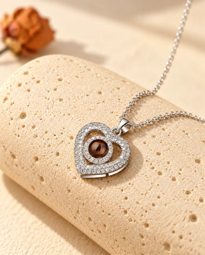 Gepersonaliseerde zilverkleurige ketting met dubbel hart van zirkonia en een bruin projectiesteentje, op travertijn