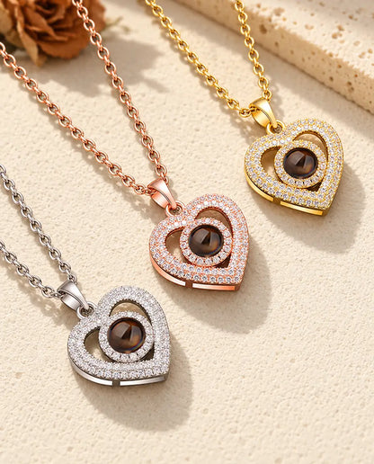 De ketting met dubbel hart en foto erin in drie kleuren, diagonaal op crèmekleurig gips