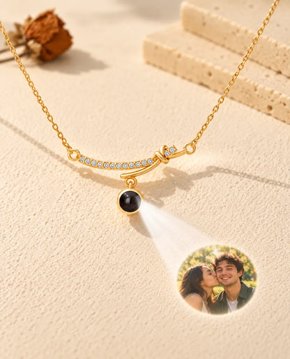 Goudkleurige ketting met gebogen staafje projecteert een foto van een stel op crèmekleurig gips