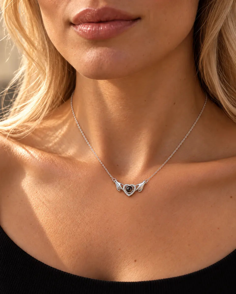 Vrouw in een zwarte gebreide top draagt de zilverkleurige ketting met handjes, hart en foto erin