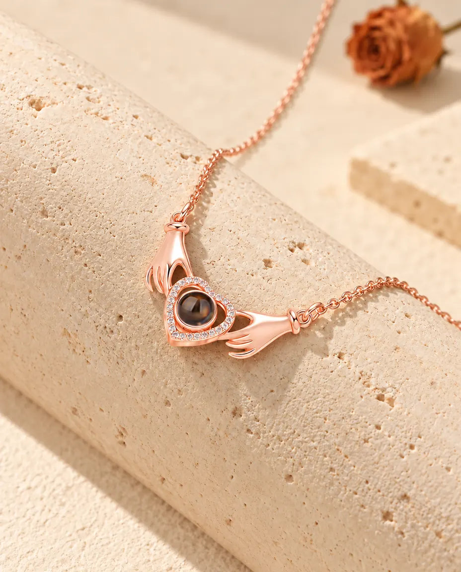 Roségoudkleurige ketting met twee handjes en een hart met foto erin, gedrapeerd over travertijn