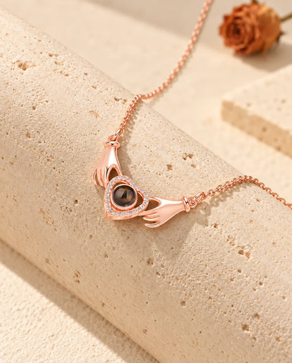 Roségoudkleurige ketting met twee handjes en een hart met foto erin, gedrapeerd over travertijn