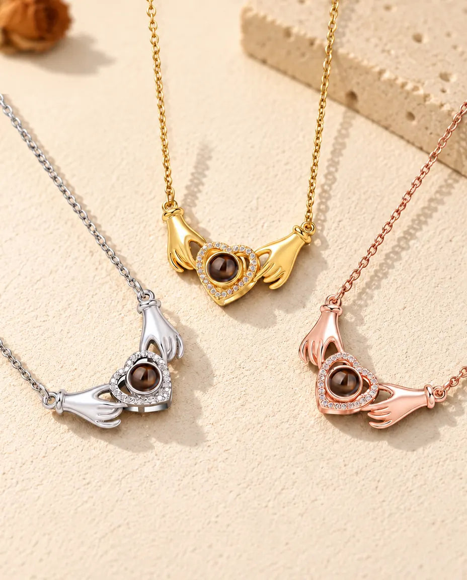 De ketting met handjes, hart en foto erin in drie kleuren op een rij op crèmekleurig gips