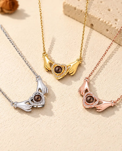 De ketting met handjes, hart en foto erin in drie kleuren op een rij op crèmekleurig gips