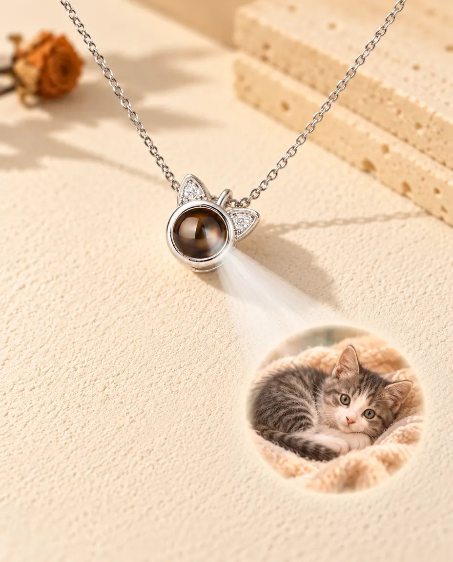 Zilverkleurige ketting met kattenoortjes projecteert een foto van een kitten op crèmekleurig gips