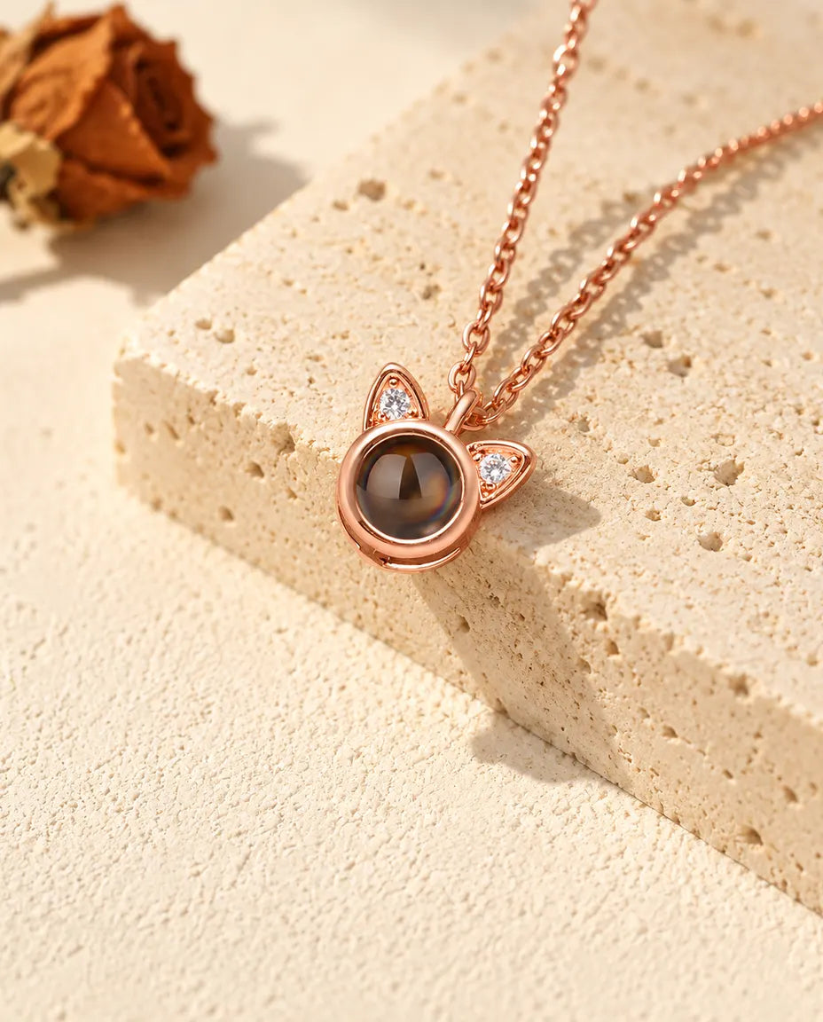 Roségoudkleurige ketting met kattenoortjes en foto erin, hangend over travertijn