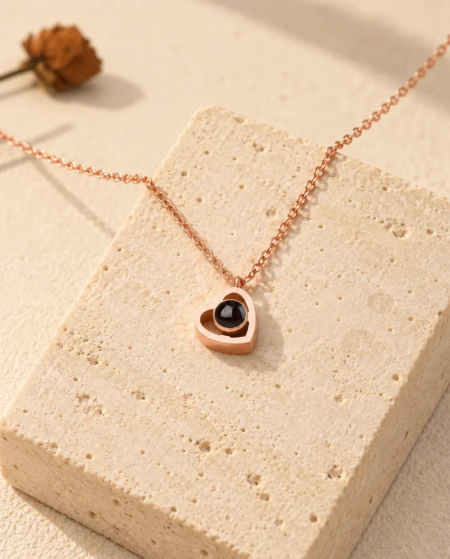 Roségoudkleurige ketting met dubbel hartje en foto erin, gedrapeerd over een blok travertin