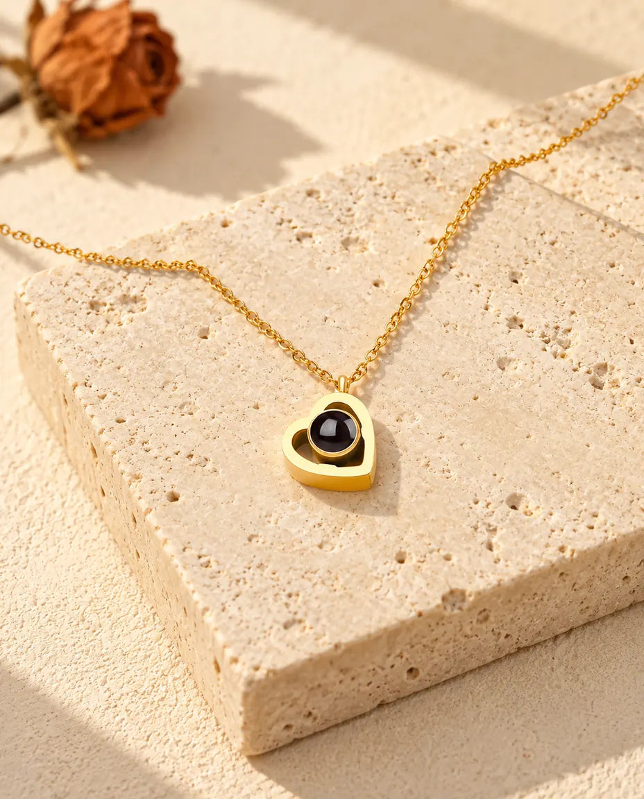 Goudkleurige ketting met dubbel hartje en foto erin, liggend op een blok travertin