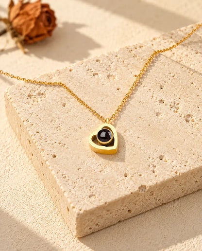 Goudkleurige ketting met dubbel hartje en foto erin, liggend op een blok travertin