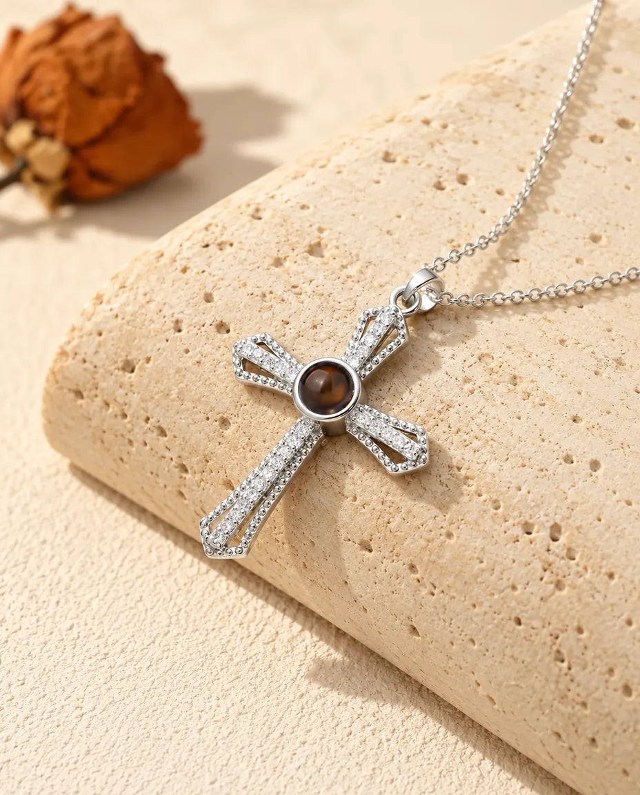 Gepersonaliseerde zilverkleurige ketting met kruis van zirkonia en een bruin projectiesteentje in het midden, op travertijn