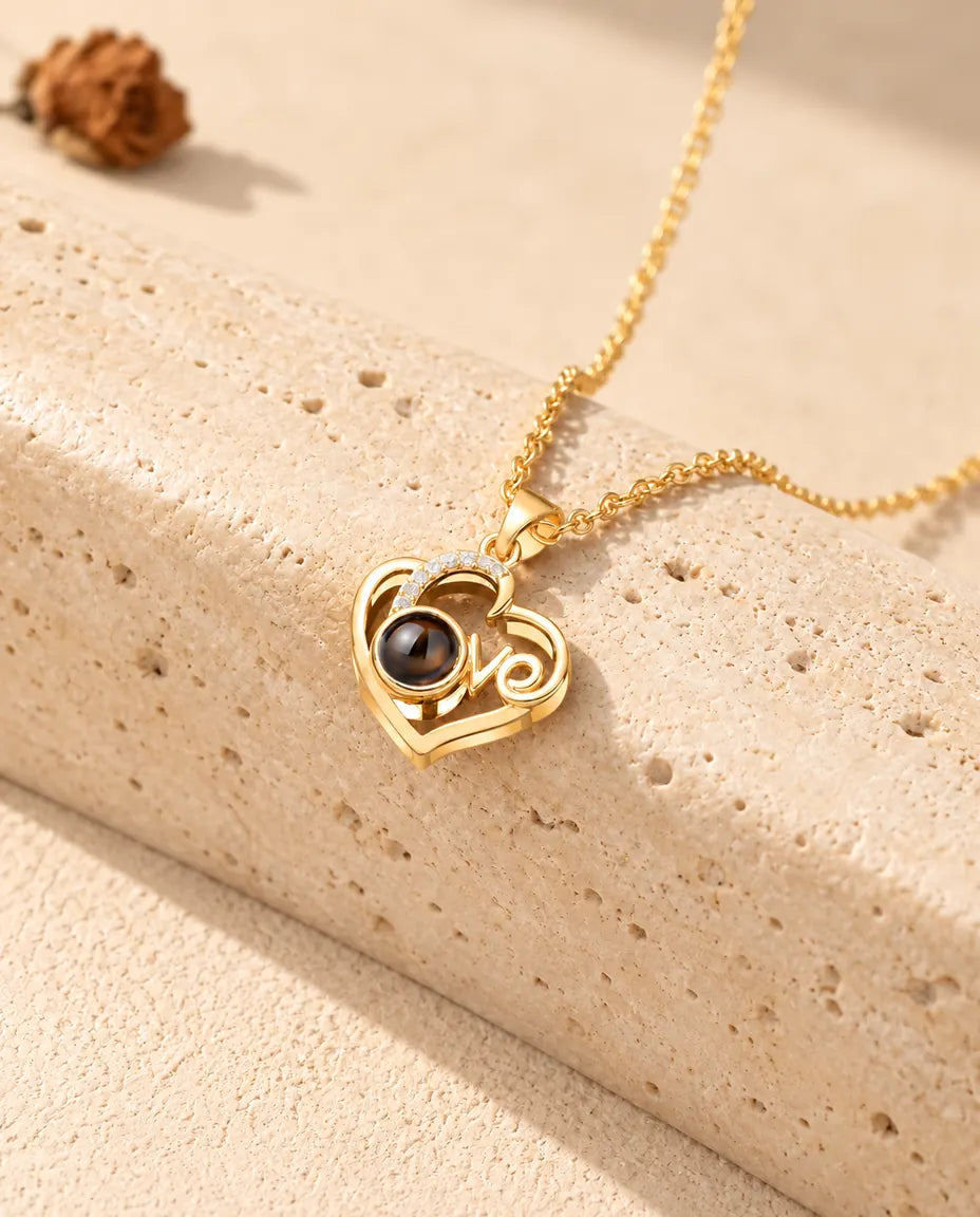 Goudkleurige Love-hart ketting met foto erin, liggend op een blok travertin
