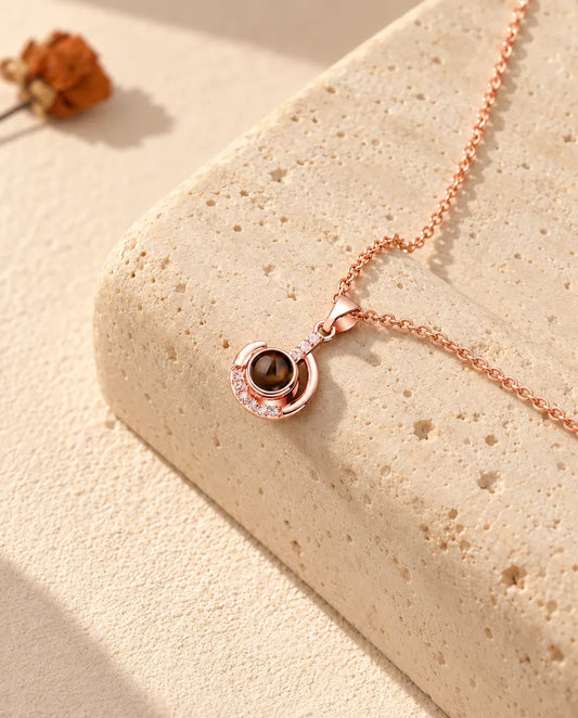 Gepersonaliseerde roségoudkleurige ketting met foto erin en maansikkel op een blok travertijn