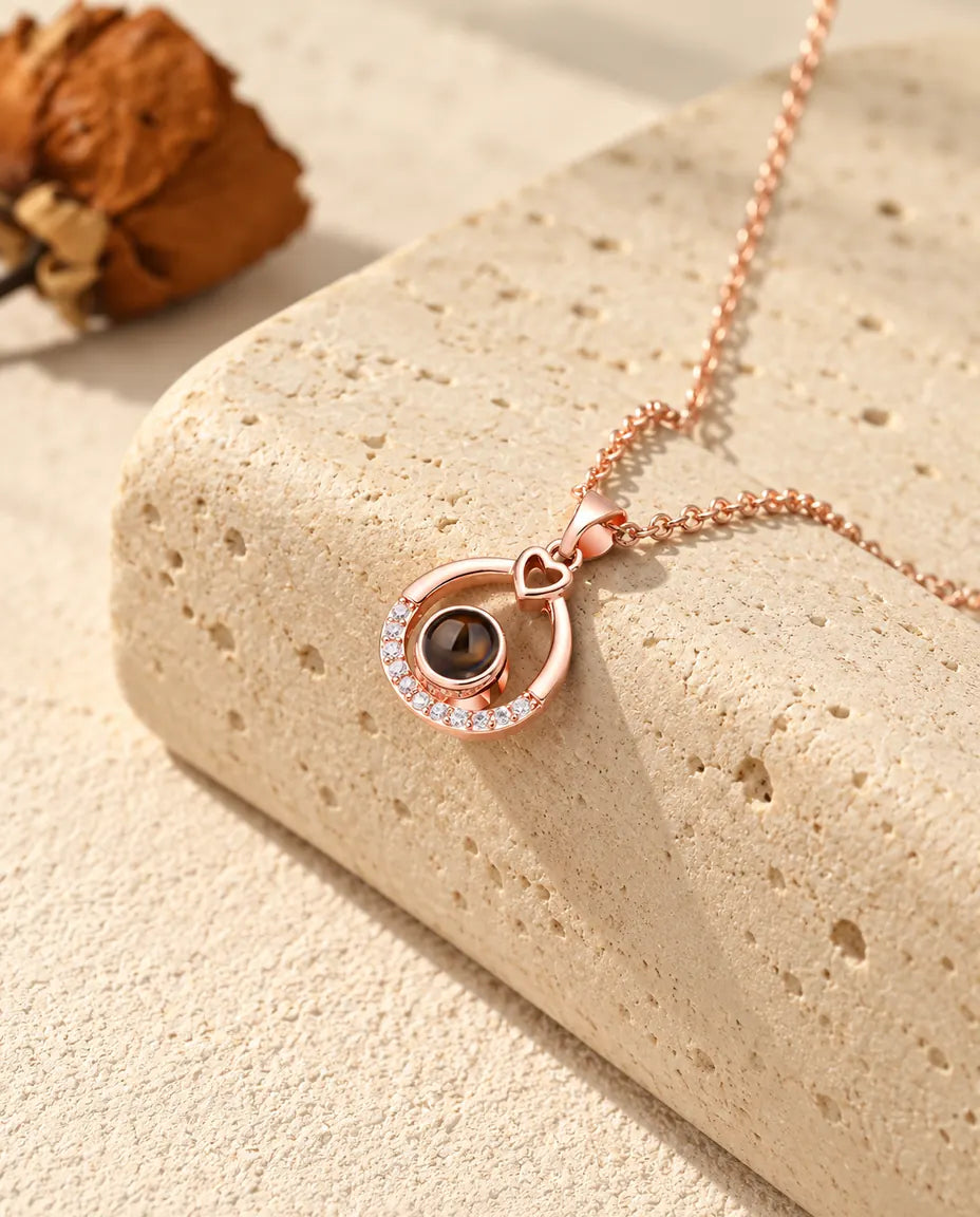 Roségoudkleurige ketting met open druppel en foto erin, hangend over travertijn