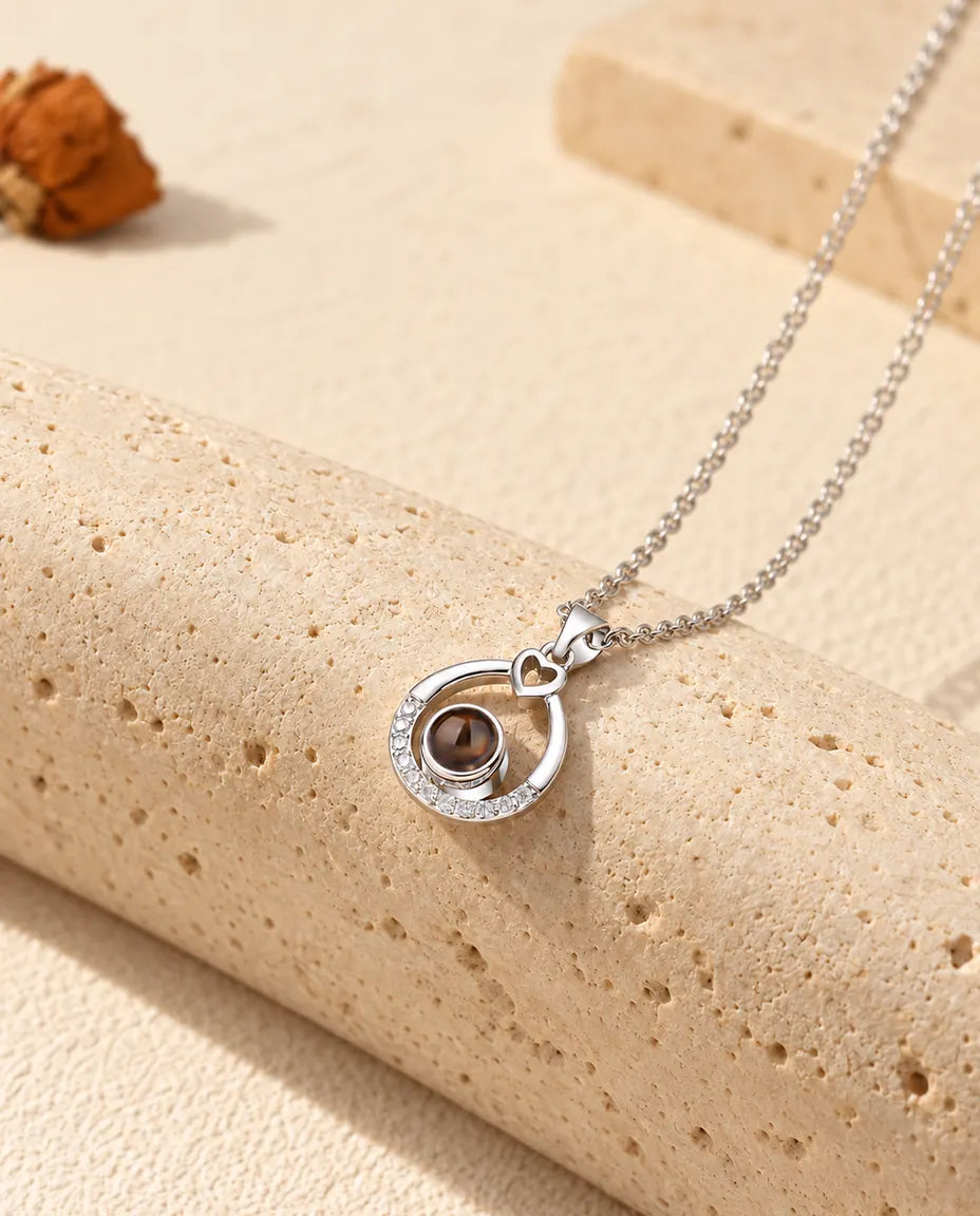 Zilverkleurige ketting met open druppel en foto erin, hangend over travertijn