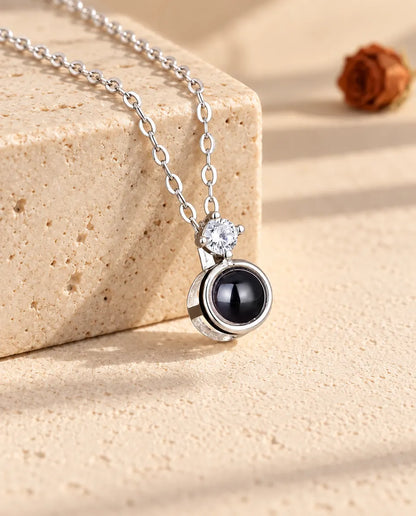 Zilverkleurige ketting met solitair en foto erin, over een blok travertijn gedrapeerd