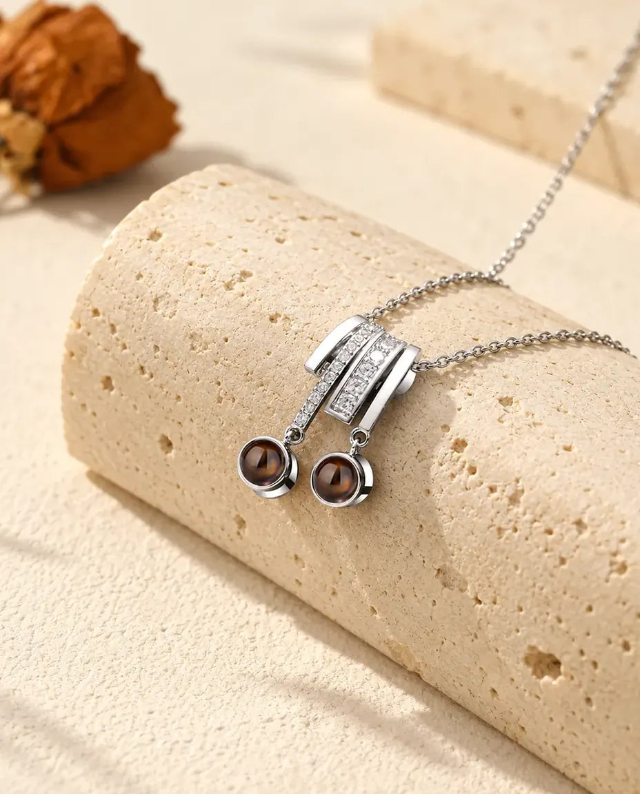 Gepersonaliseerde zilverkleurige ketting met twee foto's: schuifhanger met zirkonia en twee bruine steentjes op travertijn