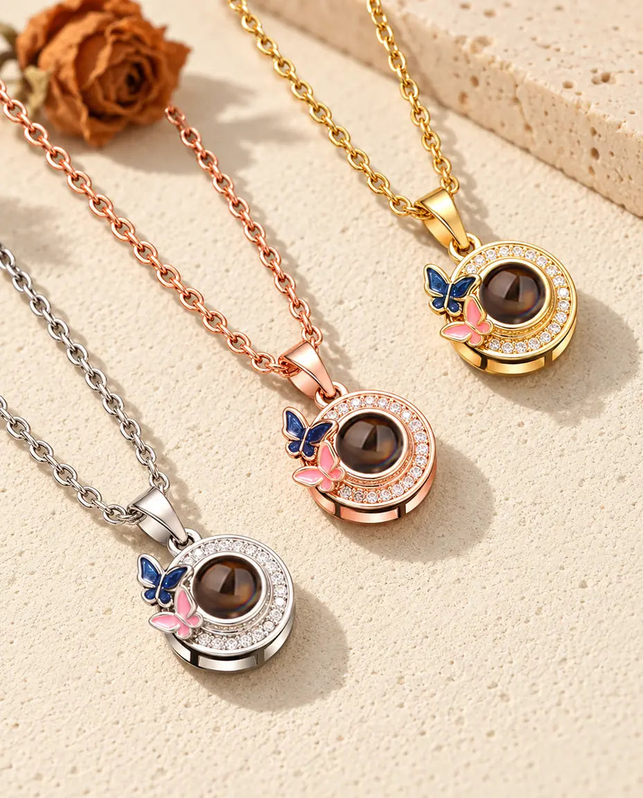 De ketting met vlindertjes en foto erin in drie kleuren, diagonaal op crèmekleurig gips