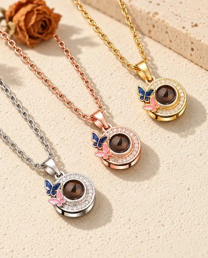 De ketting met vlindertjes en foto erin in drie kleuren, diagonaal op crèmekleurig gips