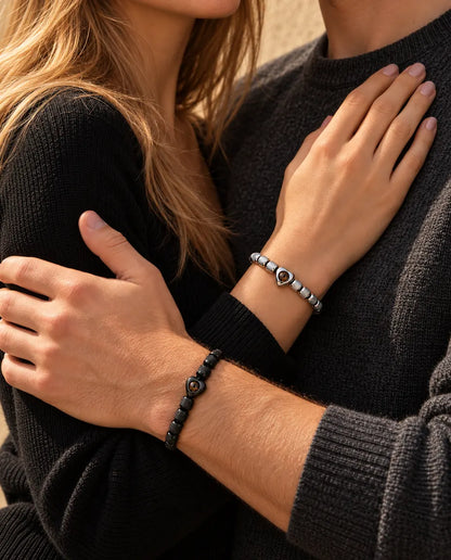 Stel in een omhelzing: zij draagt de zilverkleurige armband met hartkraal, hij de zwarte