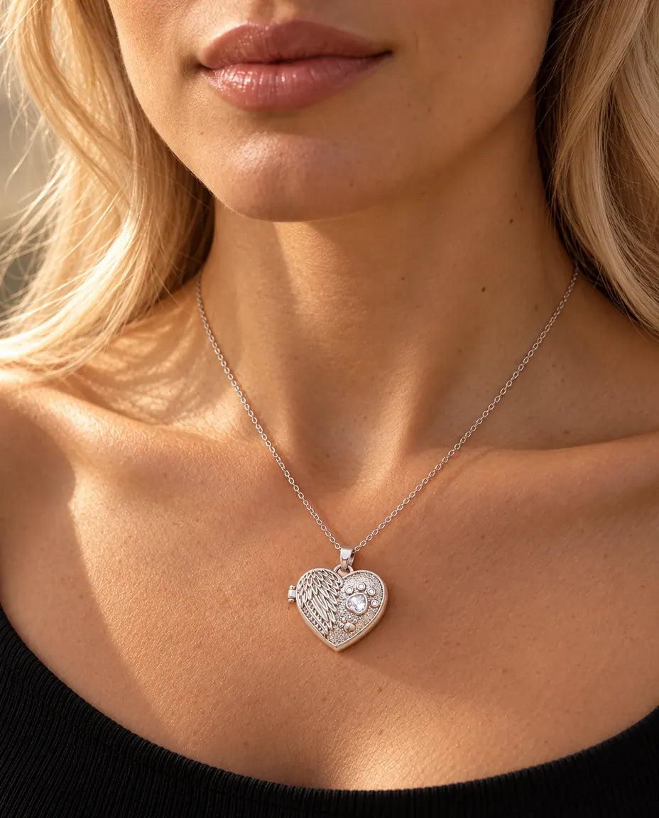 Vrouw in een zwarte gebreide top draagt de zilverkleurige ketting met hartmedaillon met engelenvleugel en poot