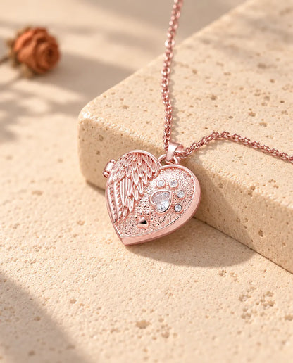 Roségoudkleurige ketting met hartmedaillon met engelenvleugel en poot op travertin in warm zonlicht