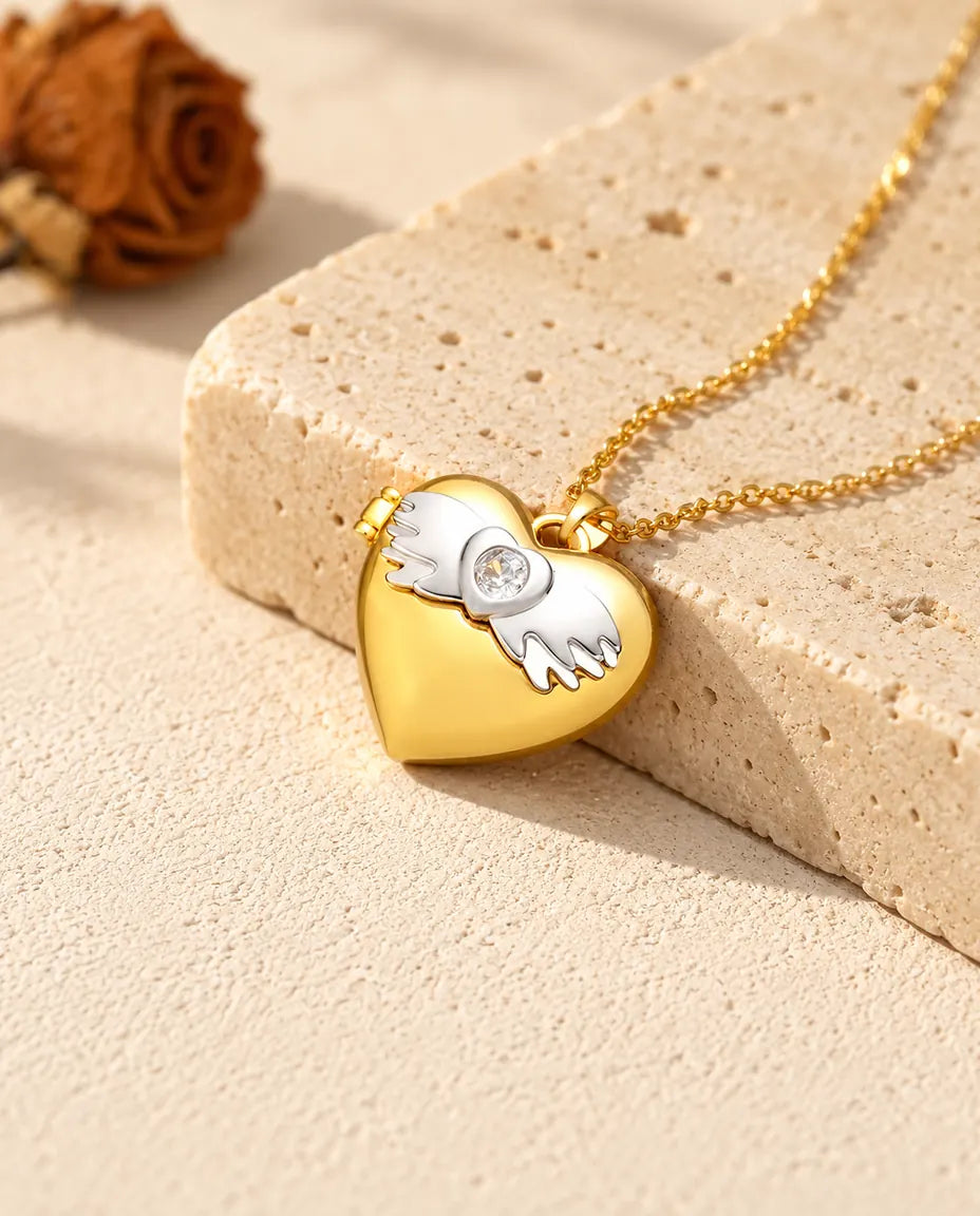Ketting met een goudkleurig hartmedaillon met vleugels, liggend op een blok travertin