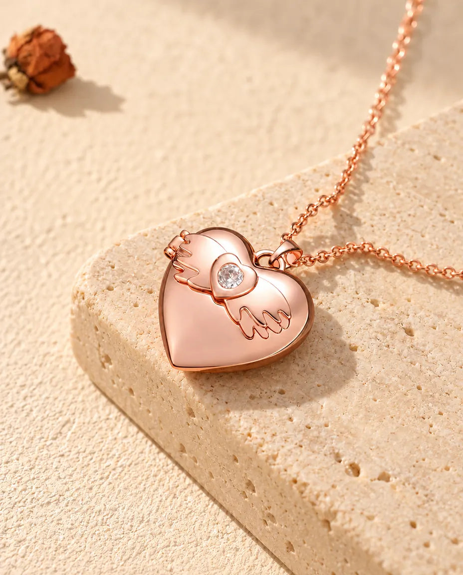 Ketting met een roségoudkleurig hartmedaillon met vleugels op travertin in warm zonlicht