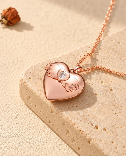 Ketting met een roségoudkleurig hartmedaillon met vleugels op travertin in warm zonlicht