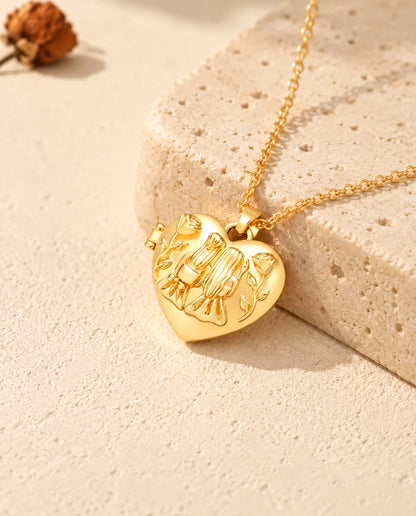 Goudkleurige ketting met hartmedaillon met twee zusjes, neergelegd op een blok travertin