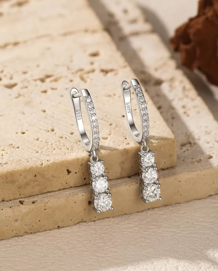 Moissanite Creolen met Drie Hangende Stenen in 925 Sterling Zilver - het paar hangend aan de rand van een travertijnplaat
