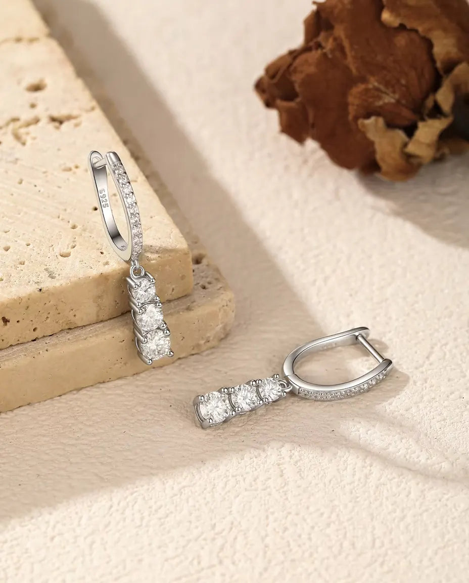 Moissanite Creolen met Drie Hangende Stenen in 925 Sterling Zilver - één oorbel hangend aan een travertijnplaat, de andere ernaast liggend