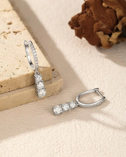 Moissanite Creolen met Drie Hangende Stenen in 925 Sterling Zilver - één oorbel hangend aan een travertijnplaat, de andere ernaast liggend