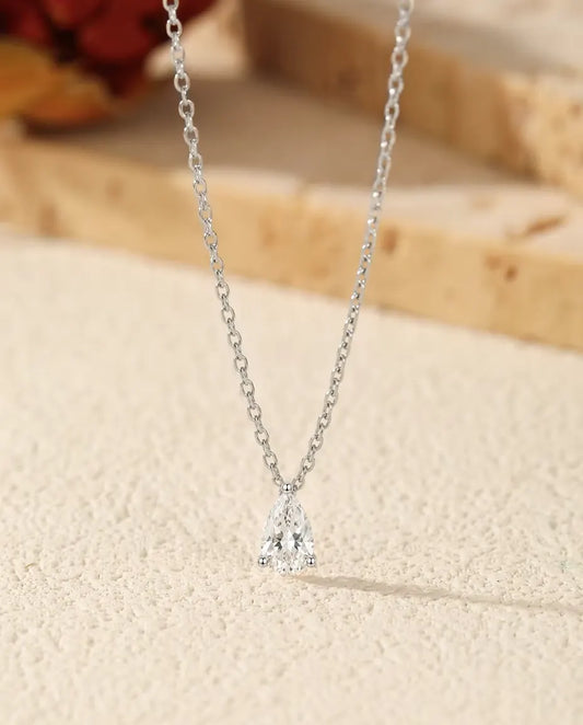 Moissanite Ketting Peervorm van 1 ct in 925 Sterling Zilver - hanger op een licht oppervlak naast een travertijnplaat