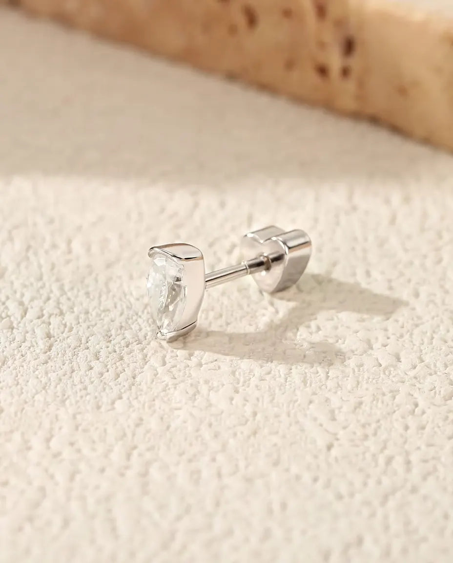 Moissanite Oorknopjes Peervorm in 925 Sterling Zilver - op een licht gestructureerd oppervlak naast een travertijnplaat