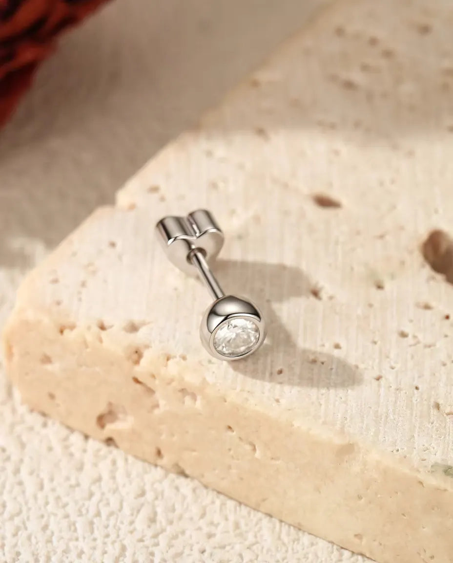 Moissanite Oorknopjes met Kastzetting in 925 Sterling Zilver - op een licht gestructureerd oppervlak naast een travertijnplaat