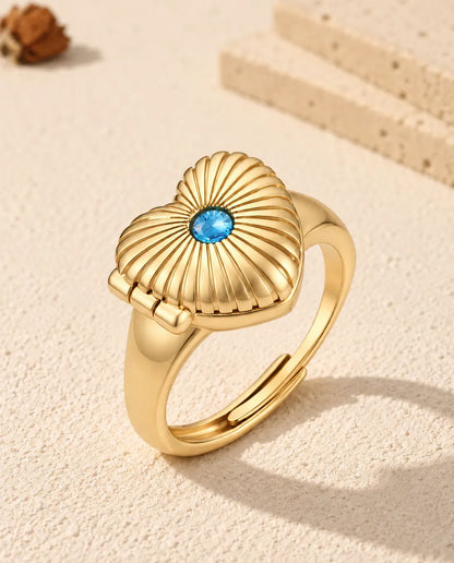 Gepersonaliseerde hartvormige medaillonring met foto in goudkleur, met een blauwe geboortesteen op het geribbelde deksel